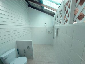 A small, enclosed bathroom with a toilet, shower, and tiled walls.