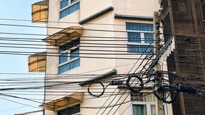 Un hotel de varios pisos con balcones, un cartel que dice 'Au Bon Hotel' y numerosas líneas eléctricas aéreas.