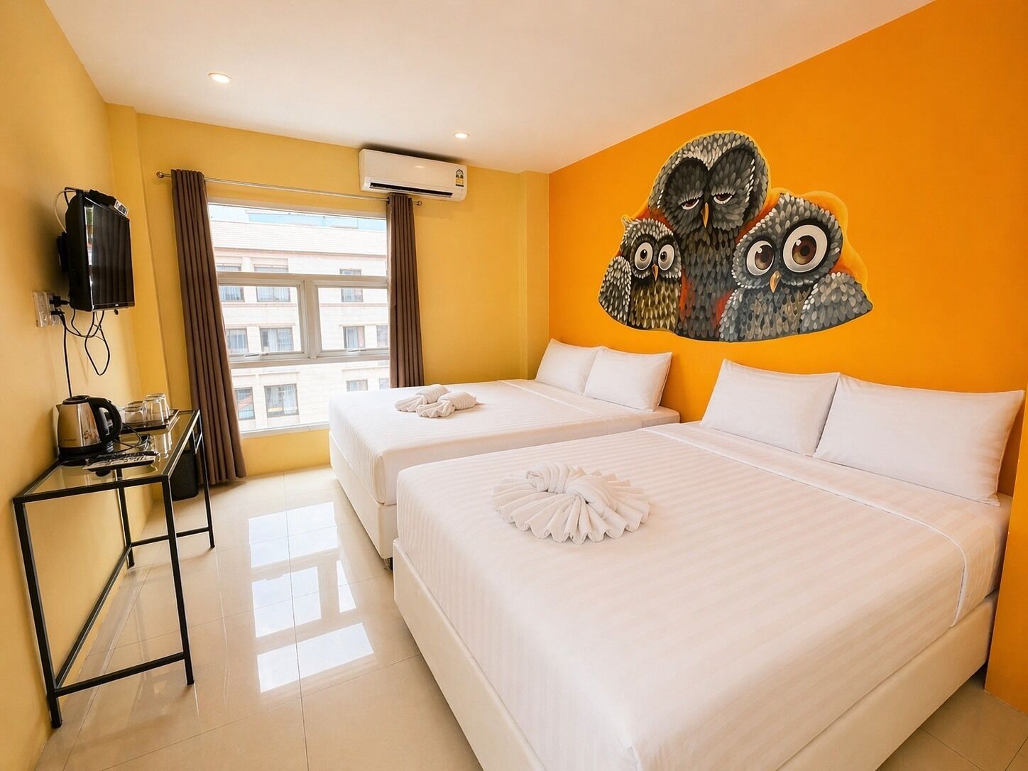 Habitación de hotel con dos camas, un televisor, una mesa con hervidor y un cuadro grande en la pared.