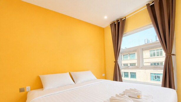 Habitación de hotel con una cama grande, ropa de cama blanca y vistas a edificios a través de una ventana con cortinas marrones.
