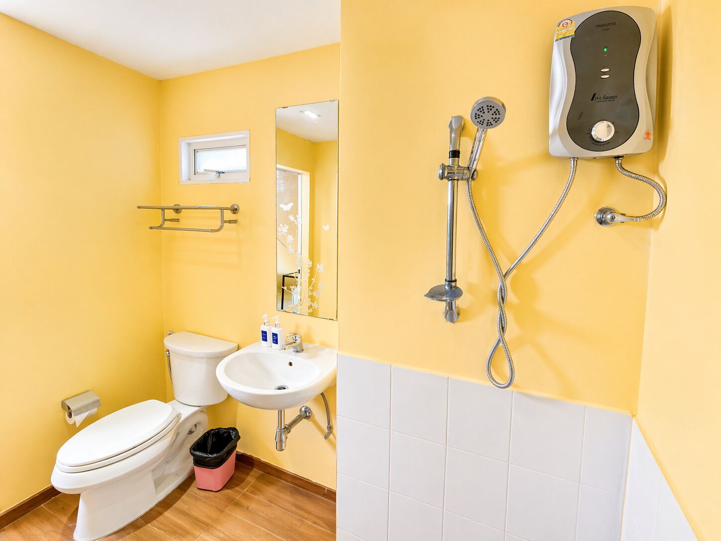 Un baño con paredes amarillas, inodoro blanco, lavamanos, espejo y cabina de ducha.