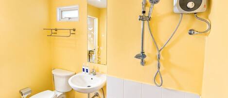 Un baño con paredes amarillas, inodoro blanco, lavamanos, espejo y cabina de ducha.
