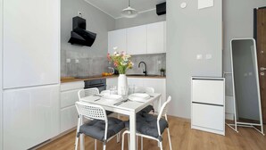 A modern kitchen with white cabinetry, a dining table set for four, and a white refrigerator. - Bright Apartment | Parking | Balcony | Remote Work (Poznań)