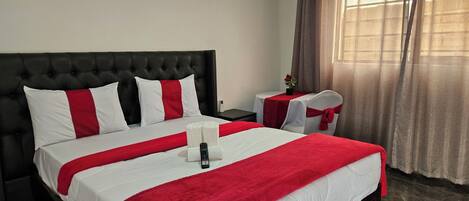 A hotel room with a large bed, a nightstand, a chair, and a window with curtains.