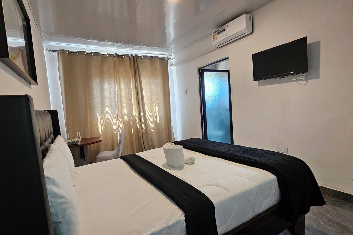 Una habitación de hotel con una cama, un televisor montado en la pared y un equipo de aire acondicionado.