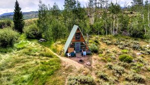 A cabin with a sloped roof, surrounded by dense forest, with a clear view of the sky. - Rustic Cabin with Spectacular Alpine Views in Walden, Colorado (Walden)