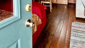 A cozy cabin interior with a wooden dining area, a small kitchen, and a bed with a red blanket. - Rustic Cabin with Spectacular Alpine Views in Walden, Colorado (Walden)