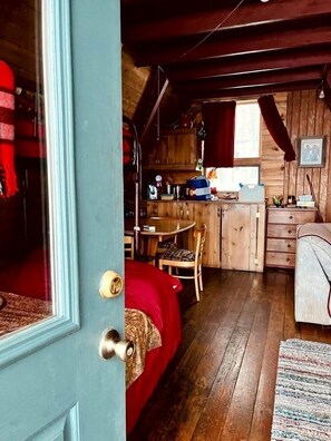 A cozy cabin interior with a wooden dining area, a small kitchen, and a bed with a red blanket. - Rustic Cabin with Spectacular Alpine Views in Walden, Colorado (Walden)