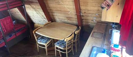 A wooden interior with a bunk bed, a round wooden table with chairs, and a sink with various items.