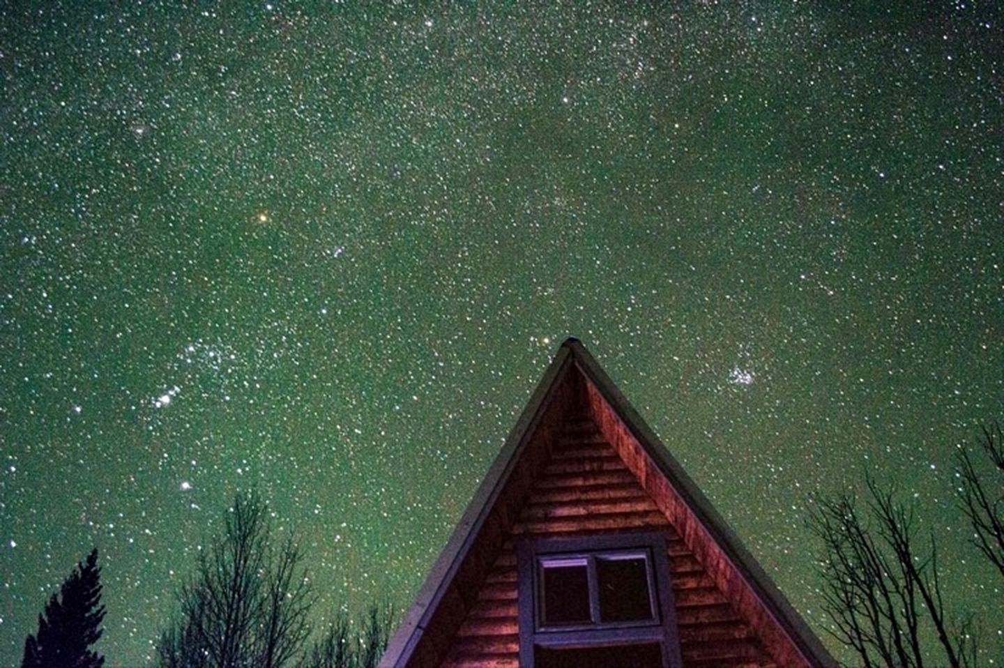 A wooden cabin with a triangular roof and a small window, set against a starry night sky.