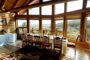 A log cabin interior with a dining table set for six, large windows, and a view of the outdoors. - Cabin Rental for Large Groups Ideal for Colorado Glamping (Walden)