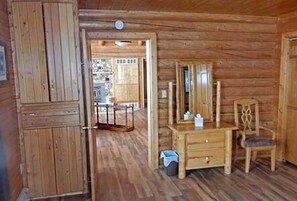 A wooden cabin interior with a dresser, mirror, chair, and a door leading to a balcony.