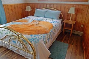 A wooden paneled room with a bed, two bedside tables, and a lamp on each.
