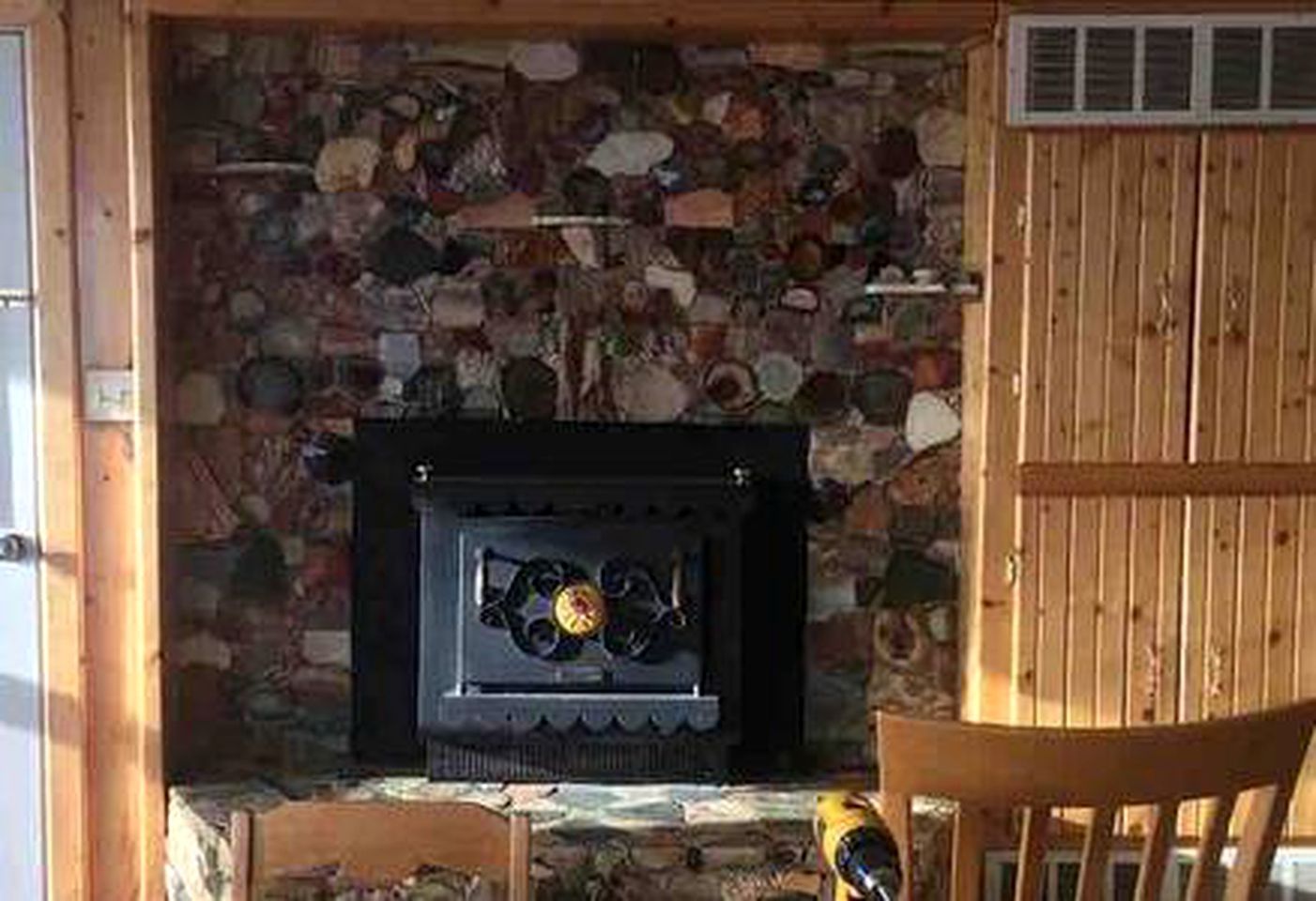 A stone fireplace with a black surround, a wooden chair, and a yellow tool on the floor.