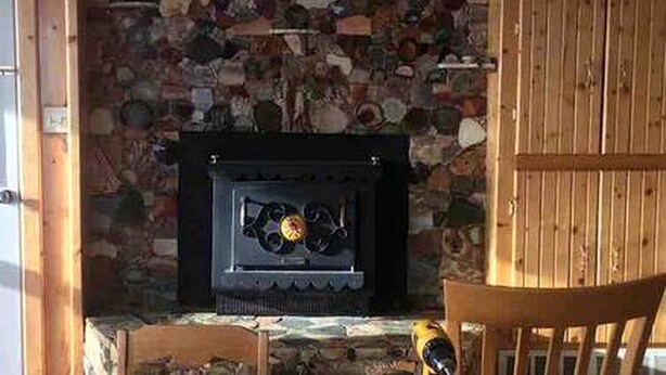 A stone fireplace with a black surround, a wooden chair, and a yellow tool on the floor. - Cabin Rental for Large Groups Ideal for Colorado Glamping (Walden)