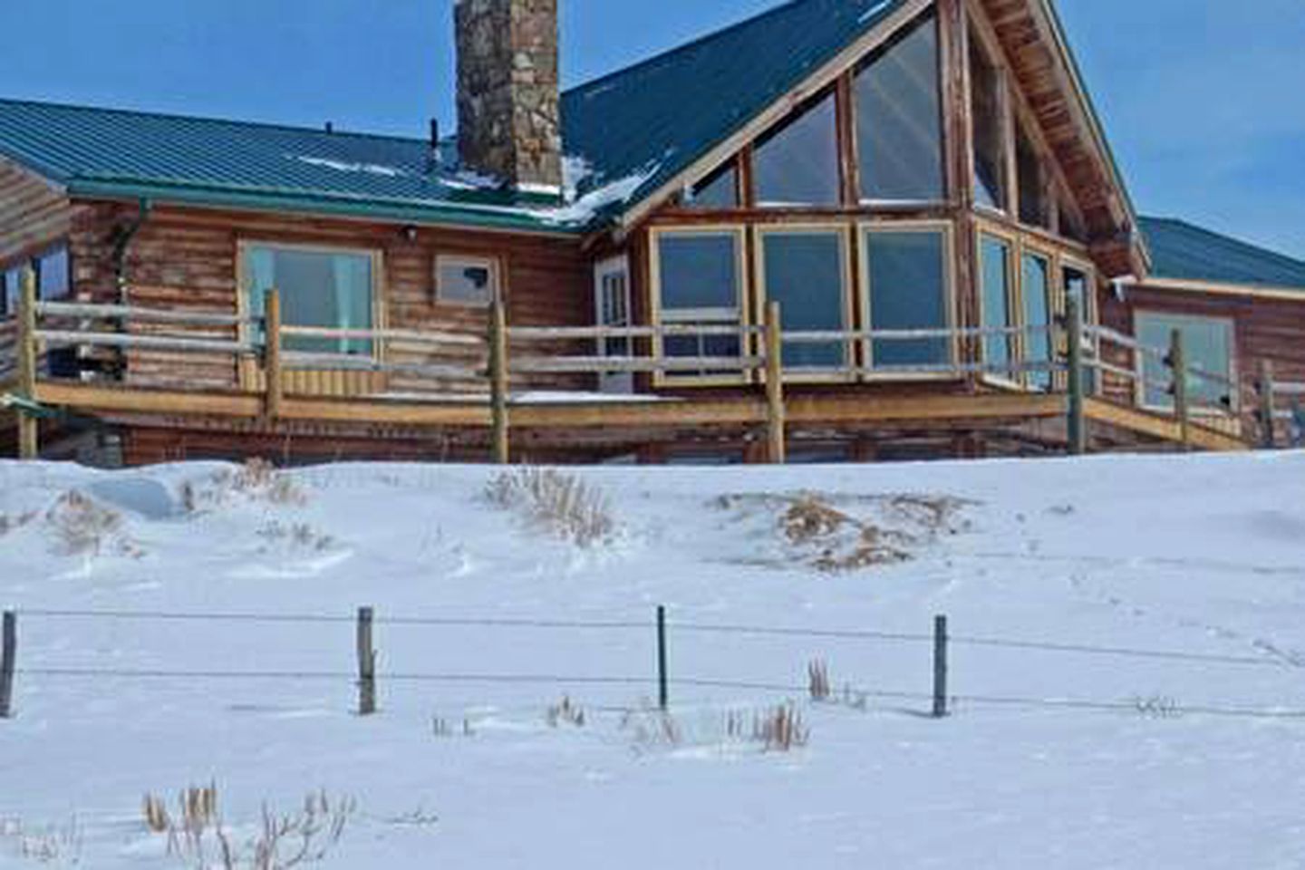 Une cabane en rondins dotée d’une grande fenêtre en verre, d’une cheminée et d’une terrasse.