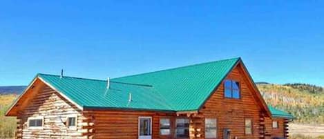 A log cabin with a green roof, a front door, and a small porch.