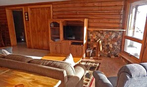 A log cabin interior with a sofa, a television, and a fireplace.