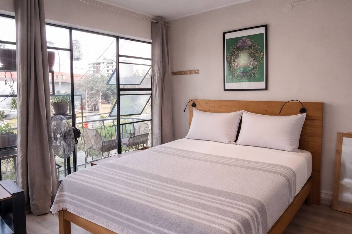 A bedroom with a bed, a ceiling fan, a window with curtains, and a view of the outside.