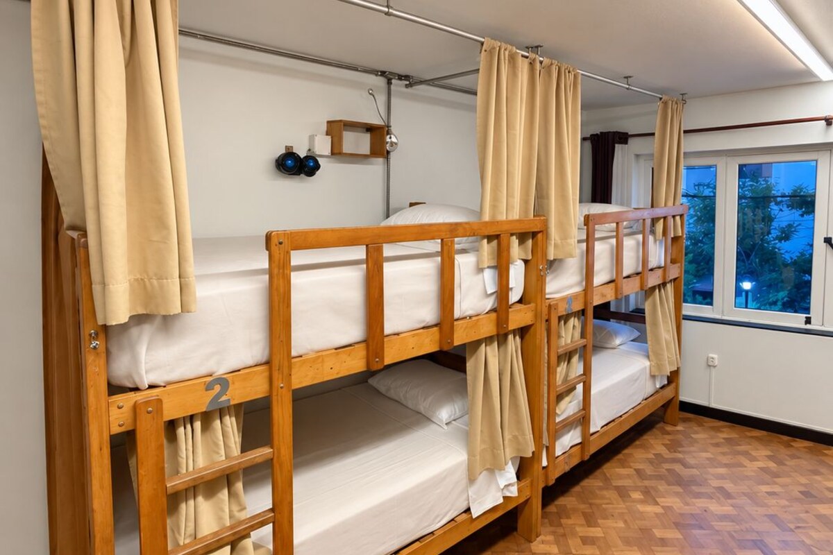 A bunk bed room with a wooden floor, a window with a view, and a ceiling light fixture.