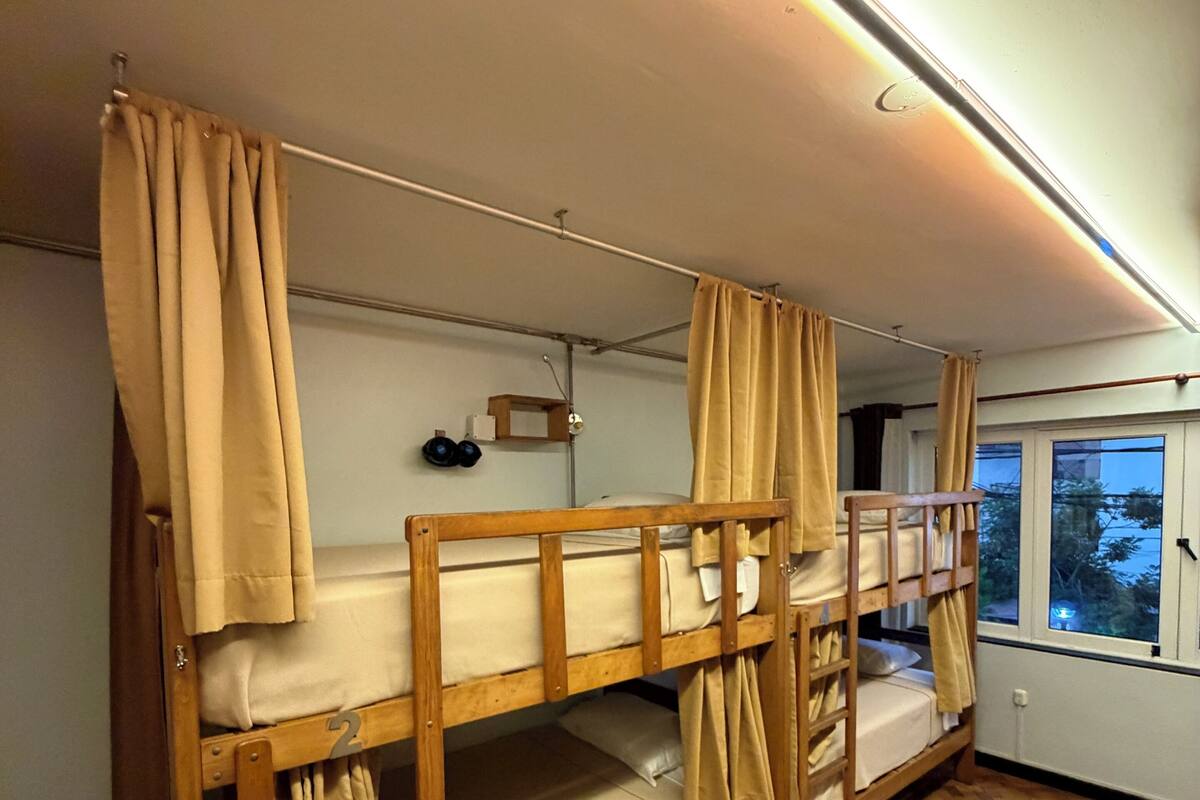 A bunk bed room with curtains, a small table with headphones, and a window with a view.