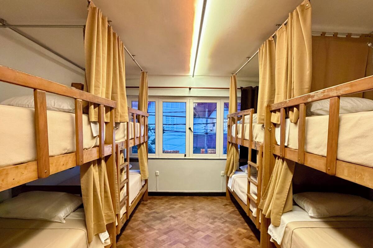 A narrow corridor with bunk beds on either side, a wooden floor, and a window at the end.