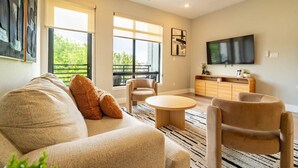 A modern living room with a sofa, armchairs, a coffee table, a TV, and a ceiling fan. - Modern Townhome | Fire Pit, Telescope, By Magnolia (Fort Worth)
