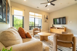 Un salon moderne comprenant un canapé, des fauteuils, une table basse, un téléviseur et un ventilateur de plafond.