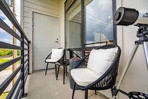 Ein Balkon mit zwei Korbstühlen, einer Kamera auf einem Stativ und einer Tür.