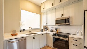 A modern kitchen with stainless steel appliances, white cabinetry, and a window providing natural light. - Modern Townhome | Fire Pit, Telescope, By Magnolia (Fort Worth)