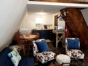 A cozy loft-style room with a dining area, kitchen, and a staircase.