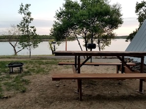 A picnic table with benches, a lamp post, and a tree in a lakeside setting.