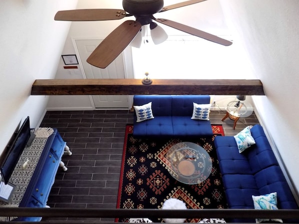 A room with a ceiling fan, a blue sofa set, a patterned rug, and a small round table.