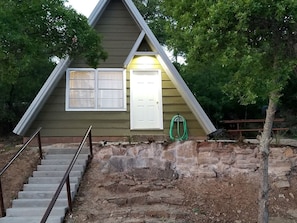 A small, single-story building with a stone foundation, a wooden exterior, and a white door.