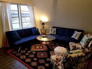 Una sala de estar con un sofá azul, un tapete estampado, una mesa de centro redonda y un sillón con estampado.