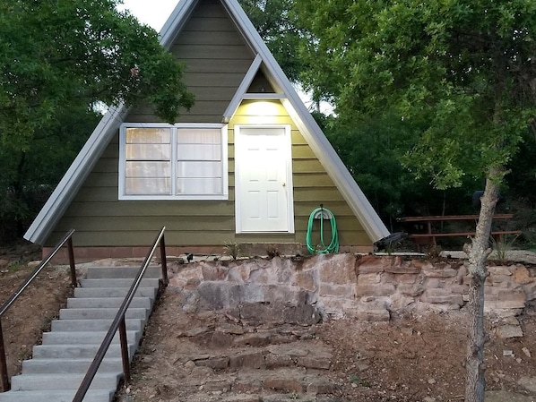 A small, single-story building with a stone foundation, a wooden exterior, and a white door.