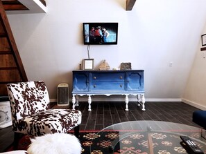 Una sala de estar con un mueble azul, un televisor montado en la pared y una alfombra estampada.