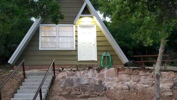 A small, single-story building with a stone foundation, a wooden exterior, and a white door.
