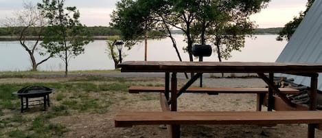 Una mesa de picnic con bancos, un farol y un árbol en un entorno junto al lago.