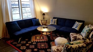 A living room with a blue sofa, a patterned rug, a round coffee table, and a patterned armchair.
