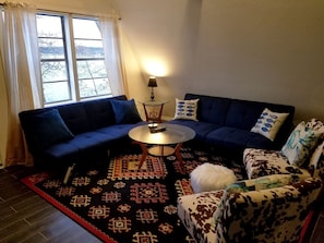 A living room with a blue sofa, a patterned rug, a round coffee table, and a patterned armchair.
