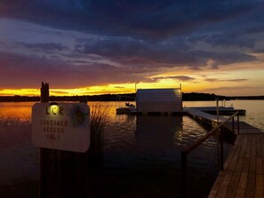 Un muelle con un letrero que indica acceso solo para clientes, un pequeño edificio y un atardecer sobre un cuerpo de agua.