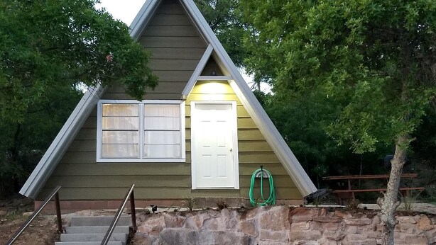 A small, single-story building with a stone foundation, a wooden exterior, and a white door.