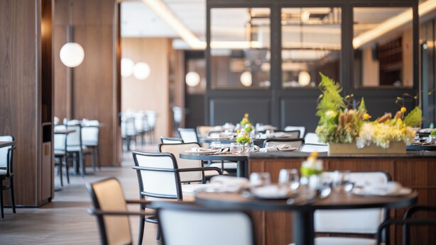 L’intérieur d’un restaurant moderne, avec des tables dressées pour le service, des lambris en bois et des luminaires suspendus.