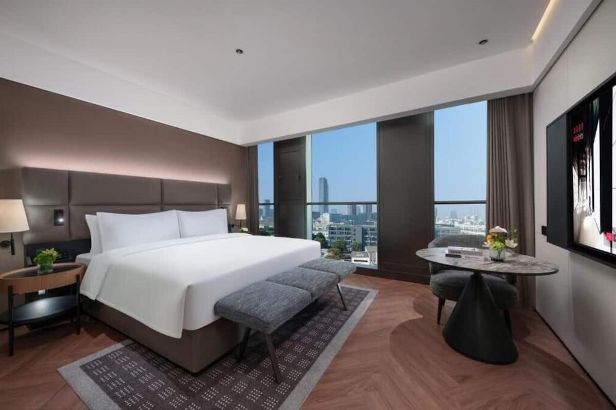 A modern hotel room with a large bed, a small table with a vase, and a city view.