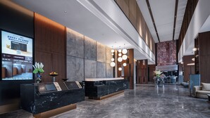 Un hall d’hôtel moderne comprenant un comptoir d’accueil, un espace salon et un grand écran numérique.