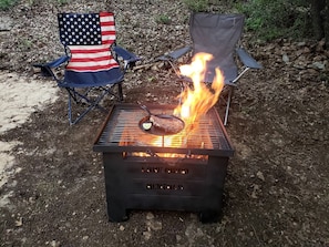 A barbecue grill with a steak cooking on it, surrounded by two chairs with American flags.
