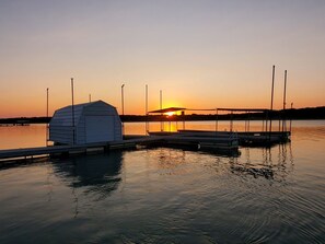 Une jetée dotée d’une structure abritée, des eaux calmes et un coucher de soleil en arrière-plan.
