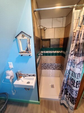 Un baño con ducha, lavabo, espejo y toallero.