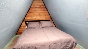 Una stanza piccola e stretta con un soffitto spiovente e un letto con testiera in legno.